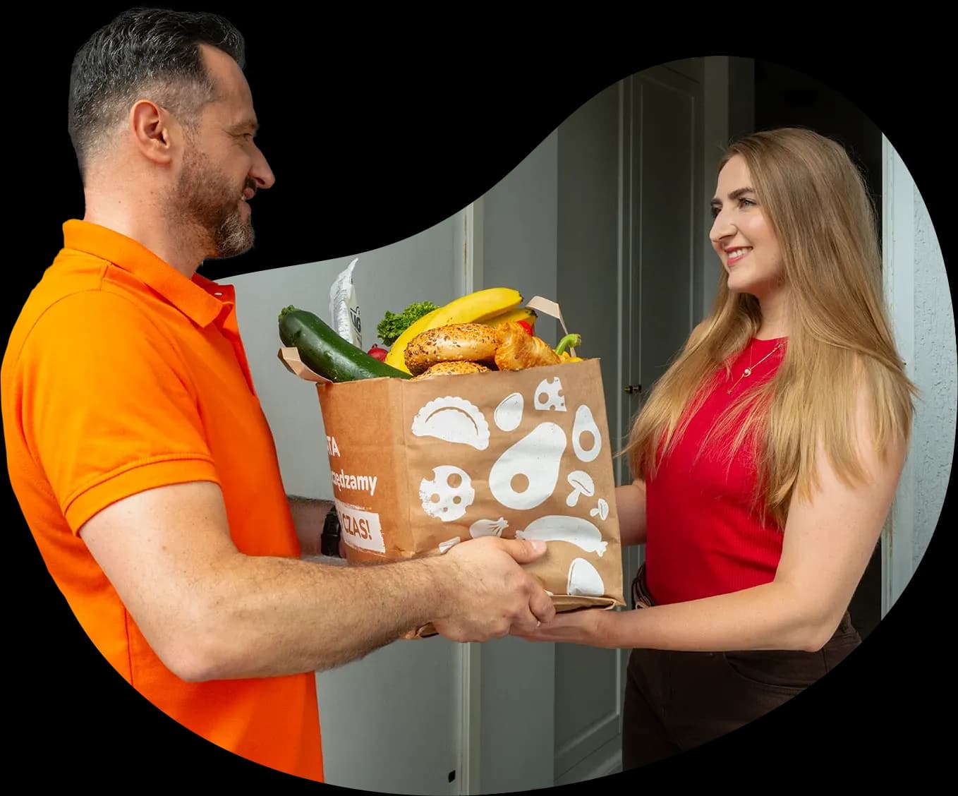 Uśmiechnięta kobieta odbiera torbę pełną zakupów od kuriera Mamyito